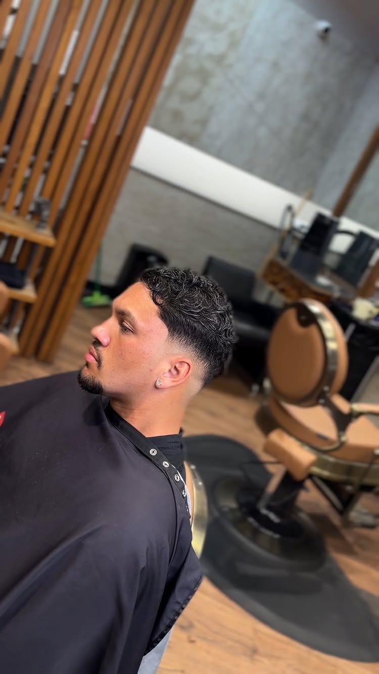 Man with a low fade haircut and curly top in a barbershop setting.