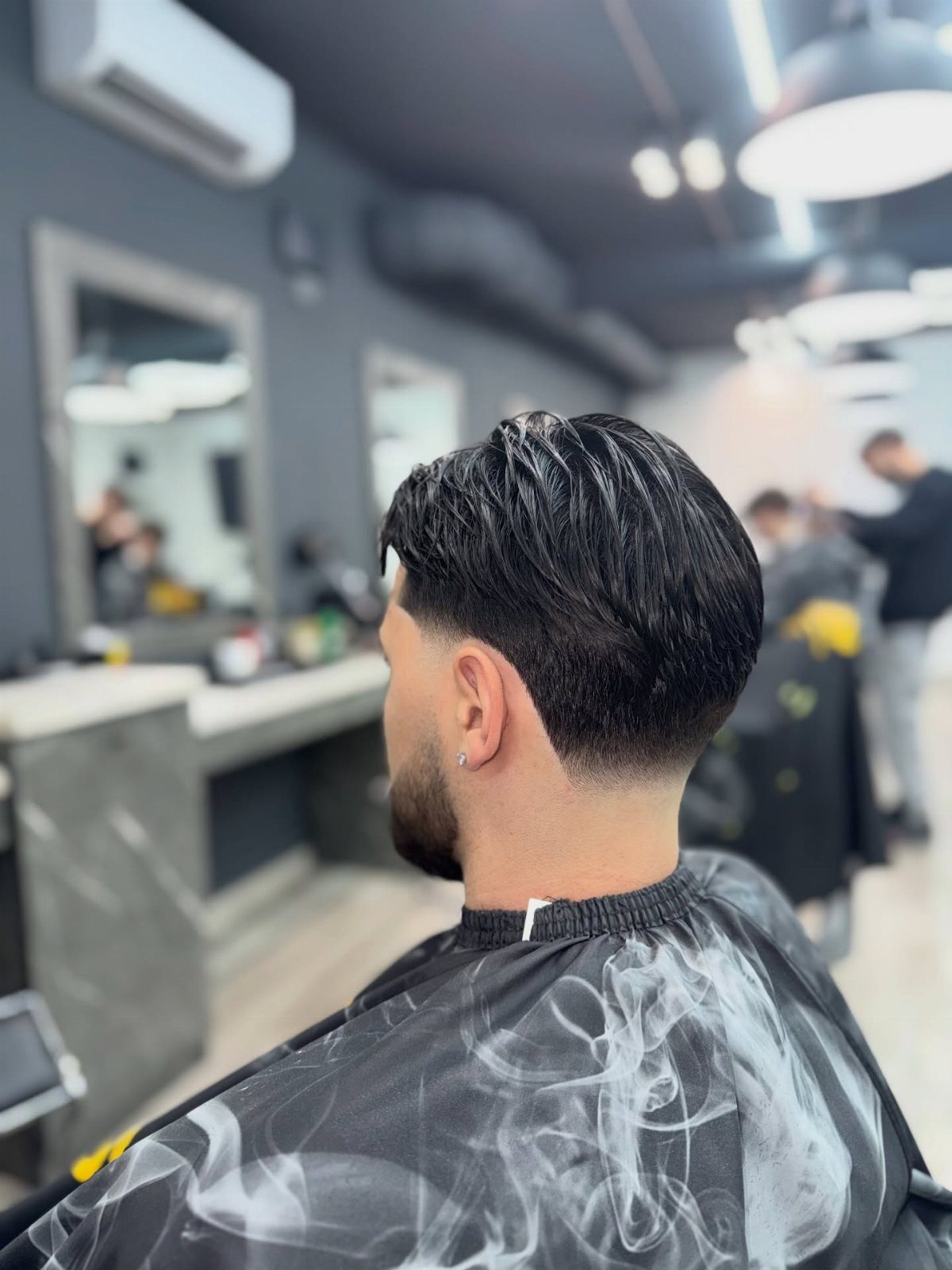 Man with a mid taper fade haircut and beard in a barbershop setting.