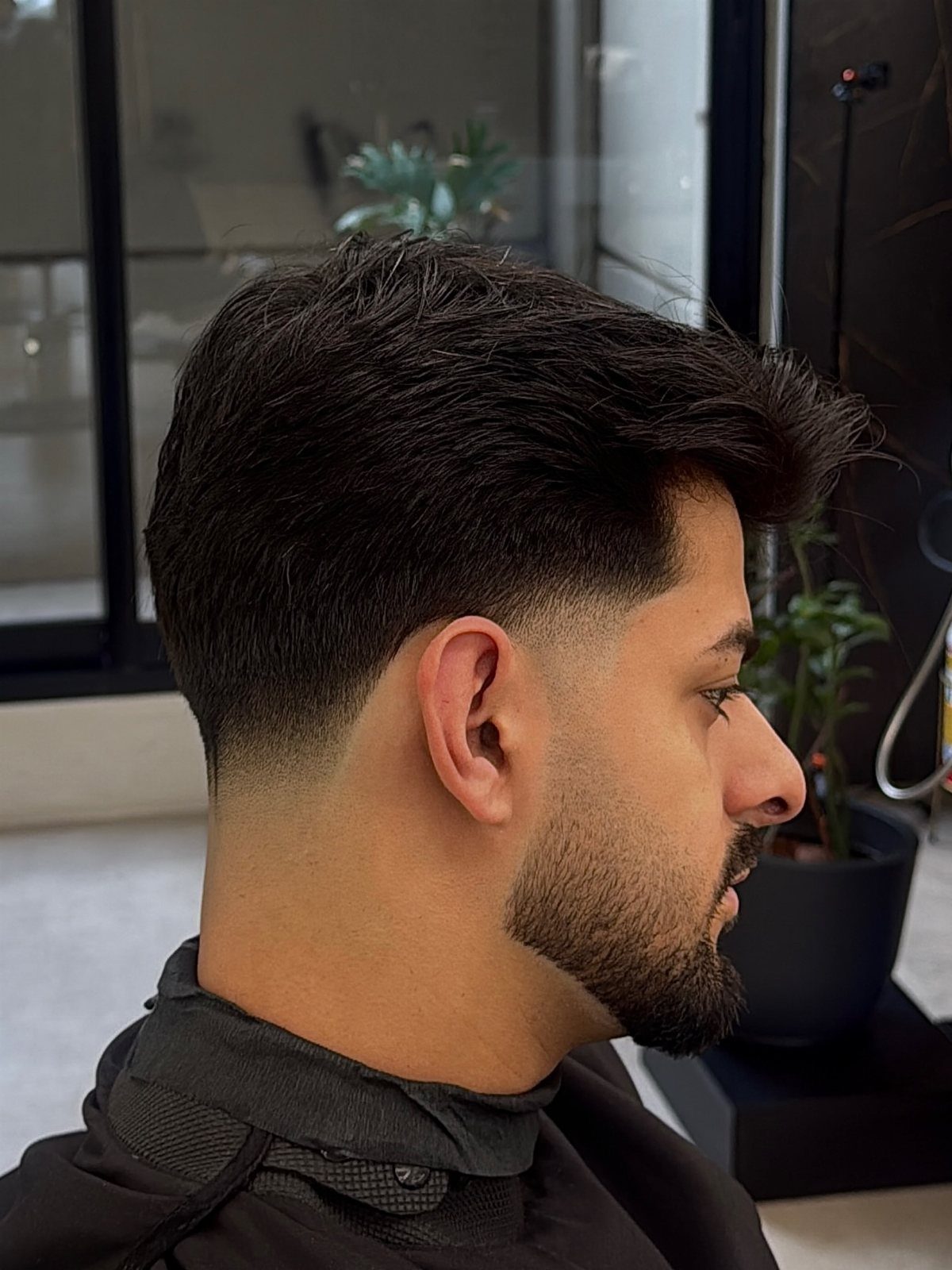 Man with a taper fade haircut and a neatly groomed beard in profile.