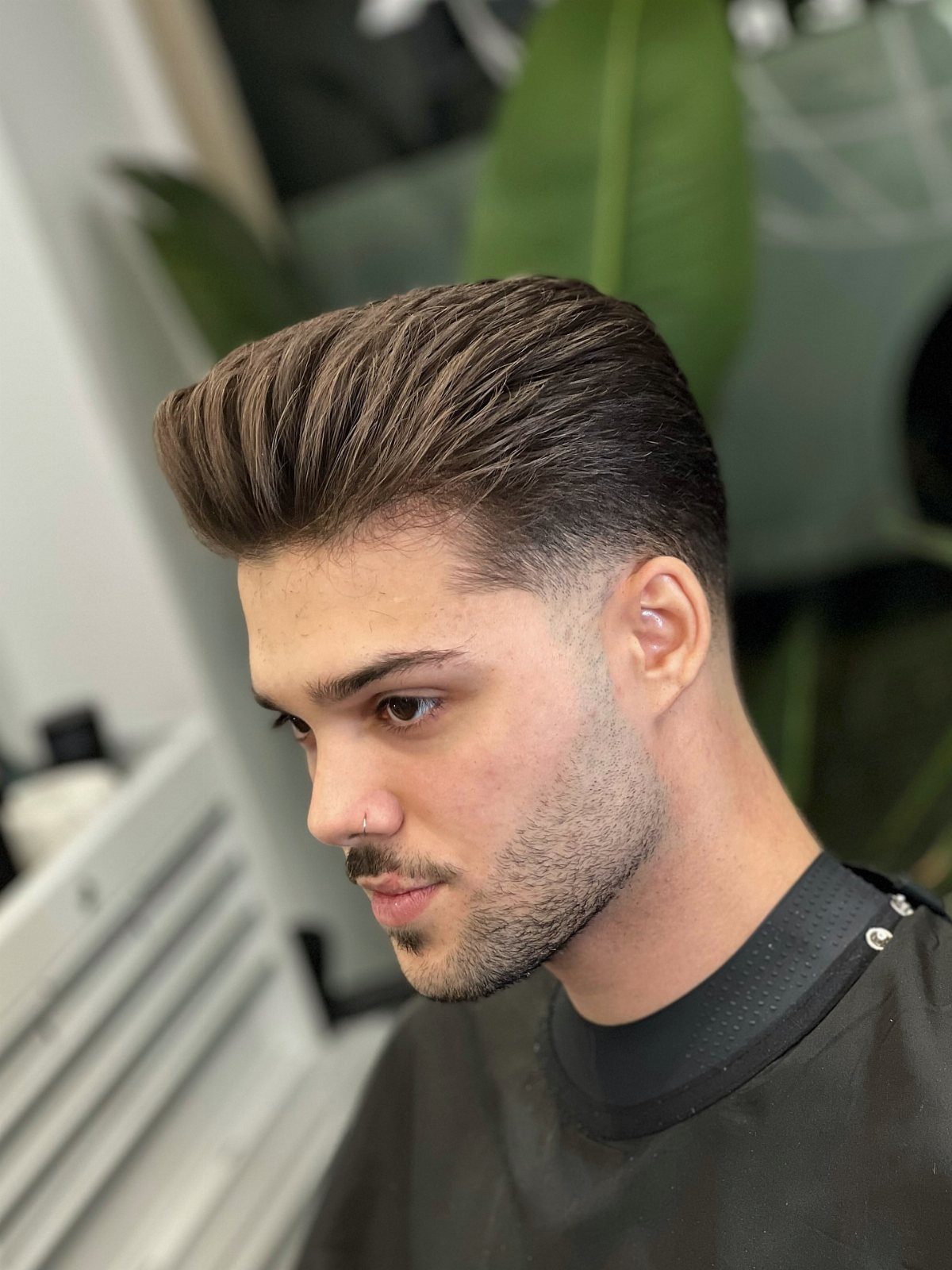 Man with a brown pompadour hairstyle and tapered fade sides in a barbershop.