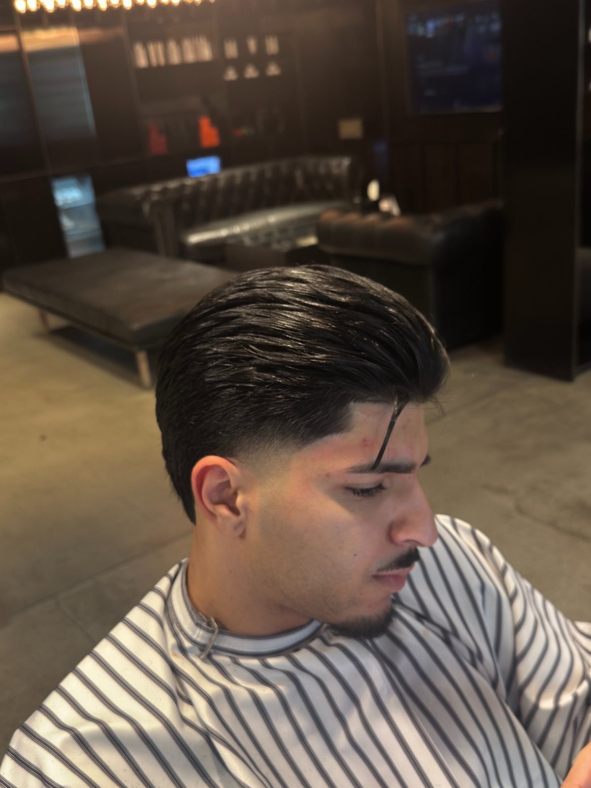 Man with a slick back hairstyle and taper fade wearing a striped cape.