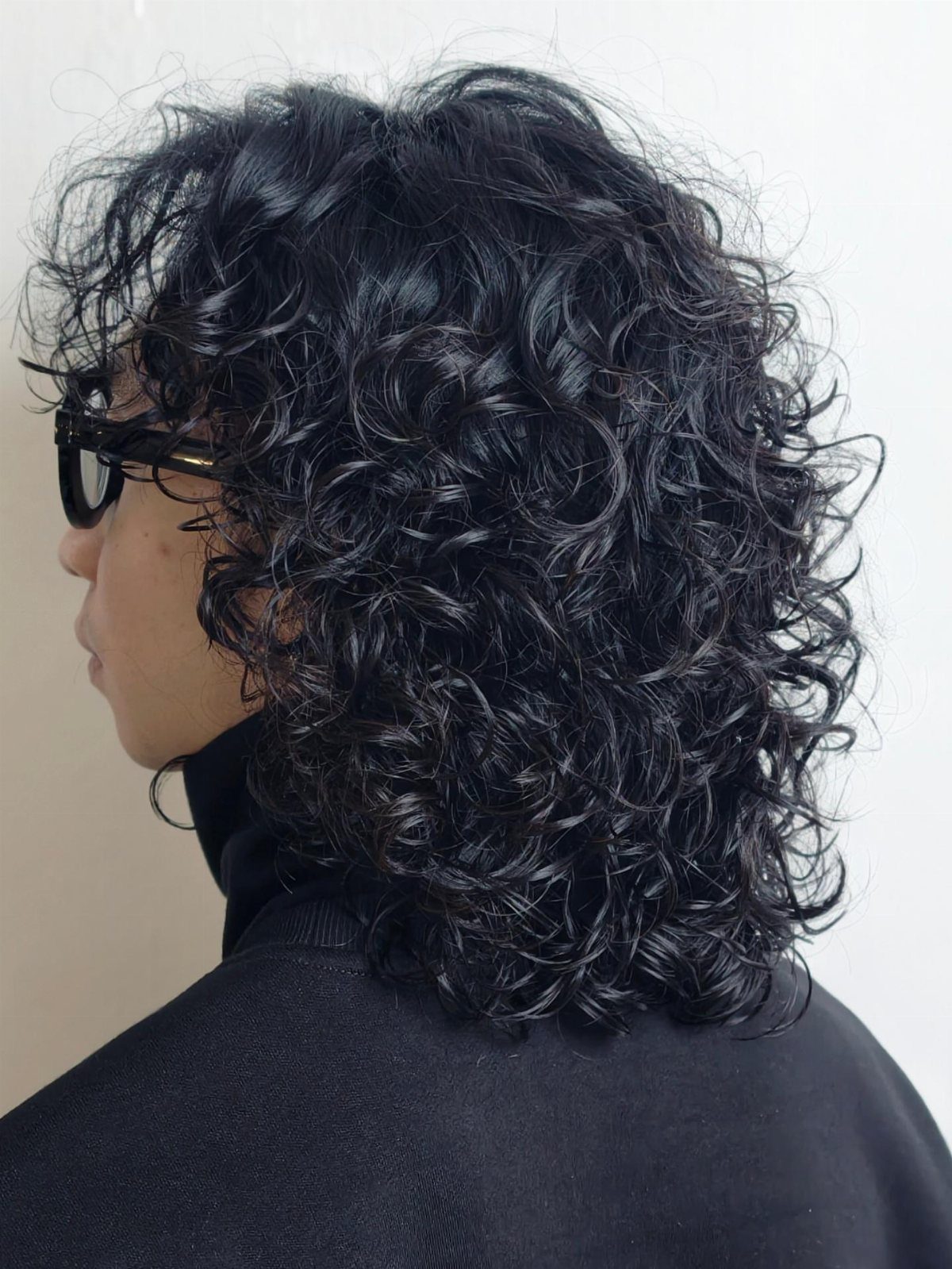 Man with curly black hair in a layered wolf cut wearing black glasses.