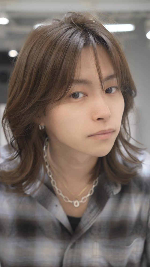 Young man with medium-length brown layered wolf cut hair wearing a plaid shirt.