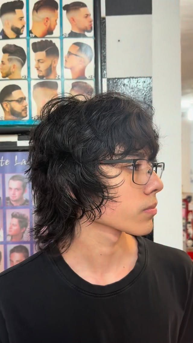 Young man with glasses sporting a shaggy black wolf cut hairstyle in a barbershop.