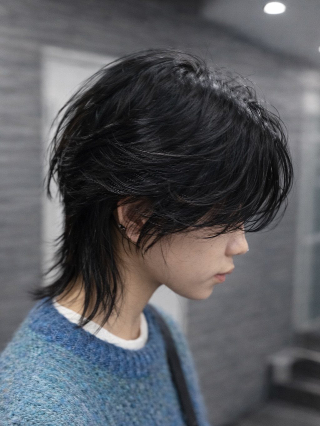 Person with a black short wolf cut hairstyle and blue knit sweater.