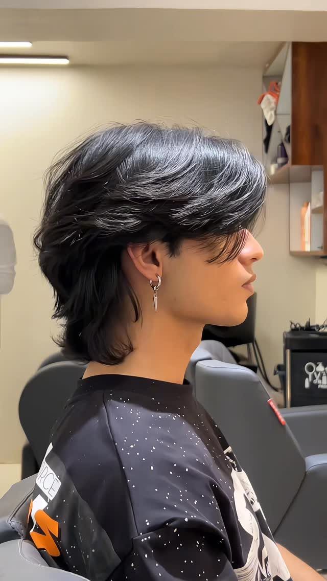 Young man with a layered black wolf cut hairstyle and a silver earring.
