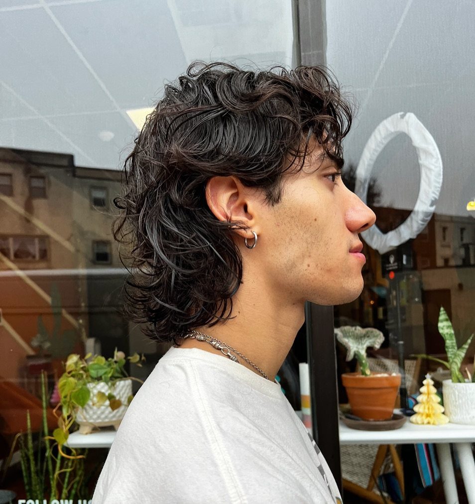 Young man with a wavy, layered wolf cut hairstyle in a side profile view
