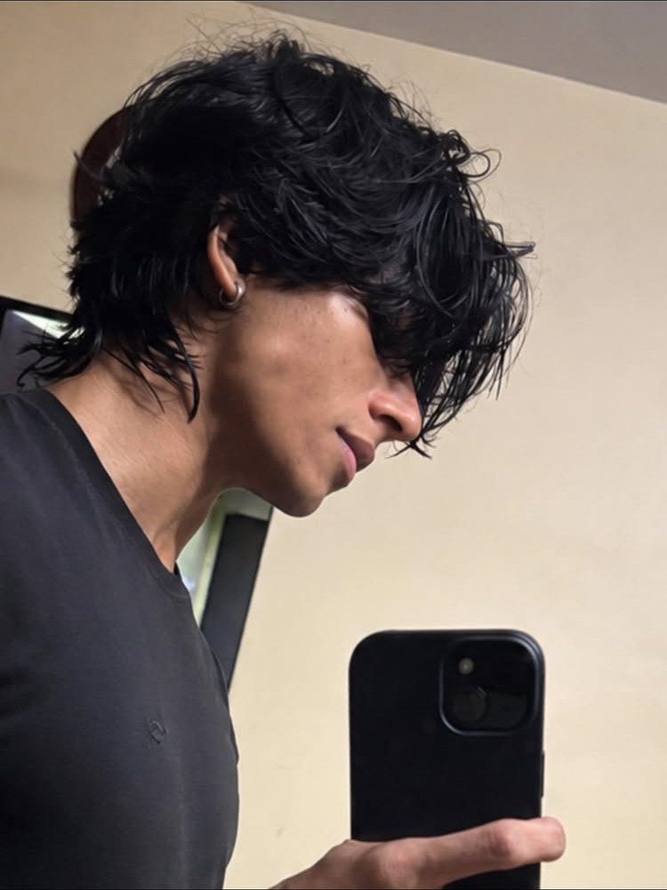 Young man with a layered black wolf cut hairstyle taking a mirror selfie.